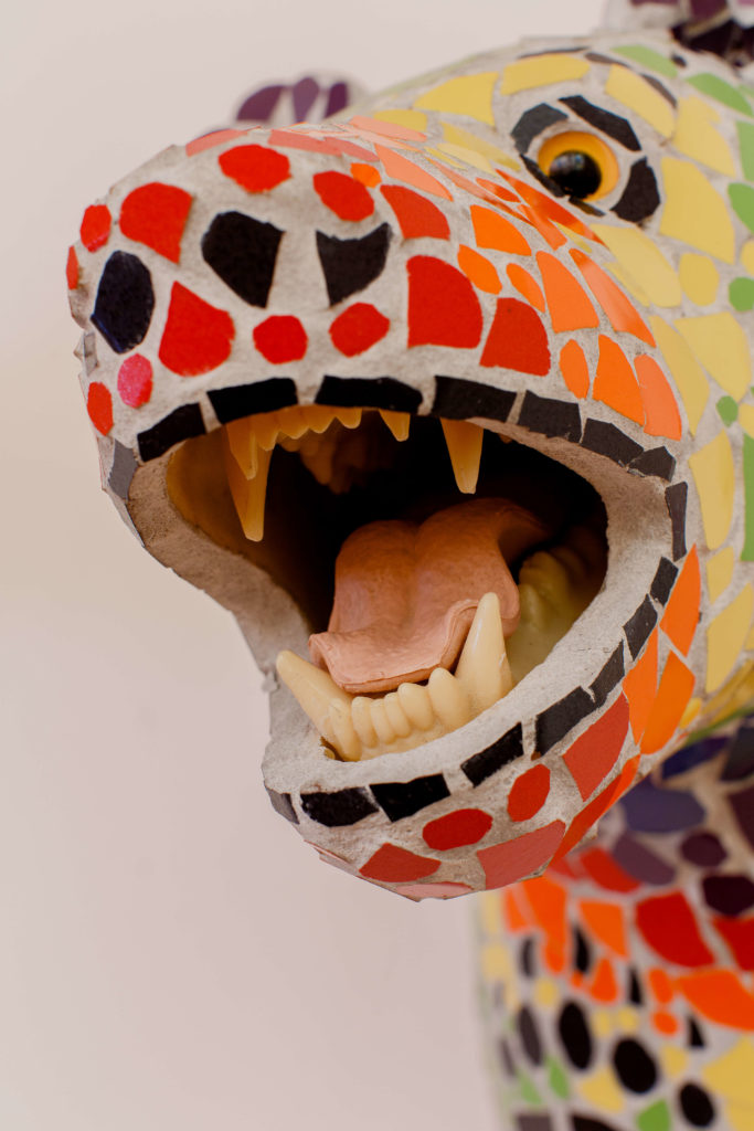 A close up view of the mouth of a bear sculpture. The bear is covered in brightly coloured tiles.