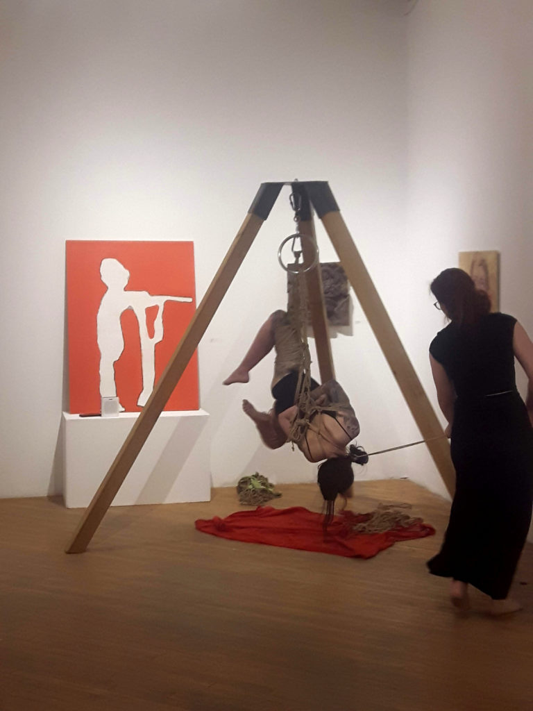 Two people performing shibari, Japanese bondage, in an art gallery.